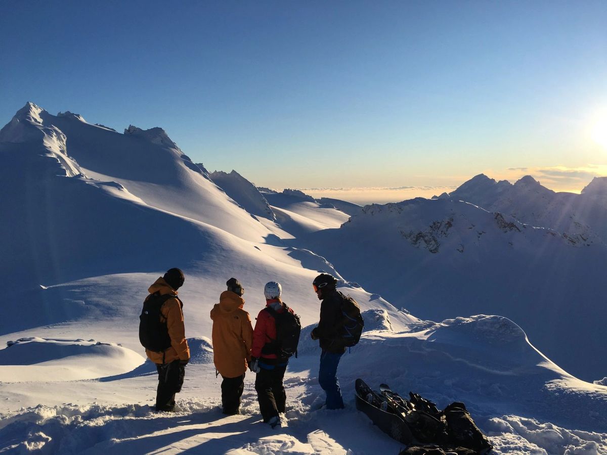 Four snowboarders standing on a snowy Alaskan summit at sunset