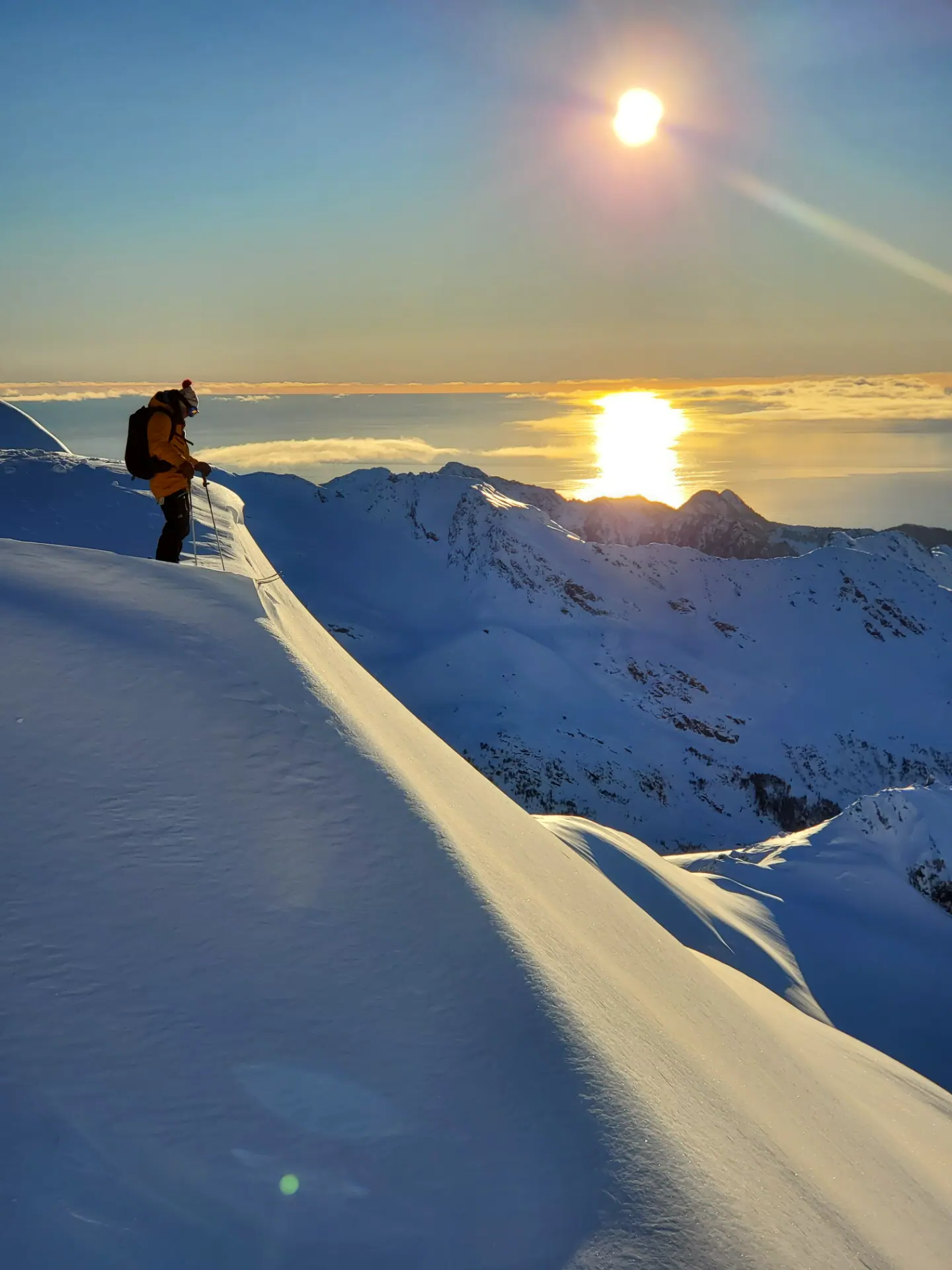 SMG guide in a yellow jacket on a steep snow-covered Alaskan ridgeline with sunlit ice formations