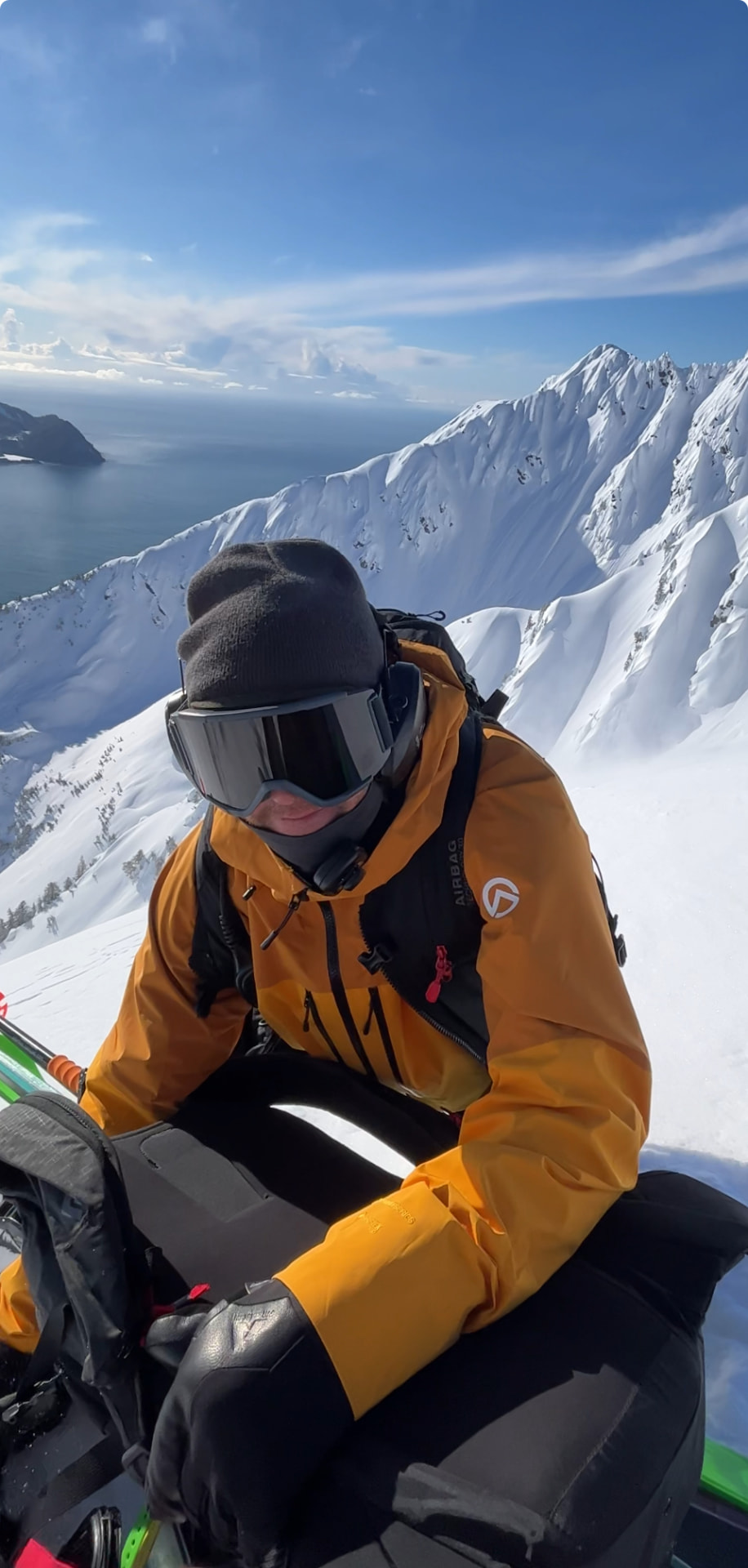 SMG snowboard guide in a yellow jacket and reflective goggles against a snowy Alaskan peak