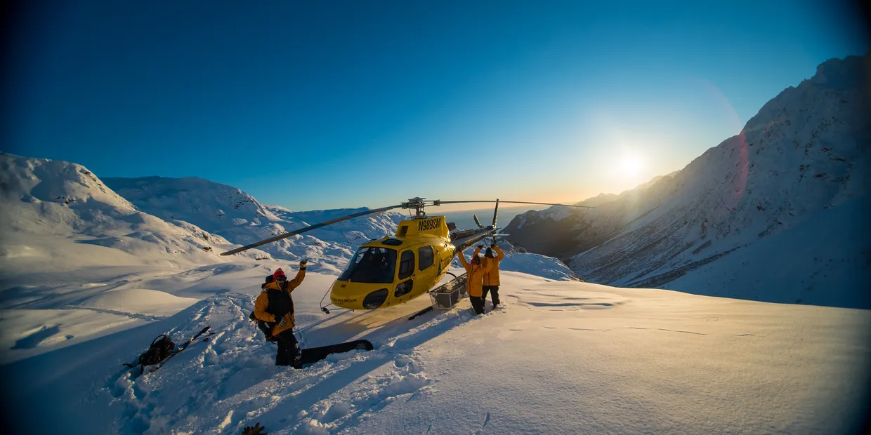 SMG helicopter landed on a snowy Alaska ridge at sunrise with guides unloading gear