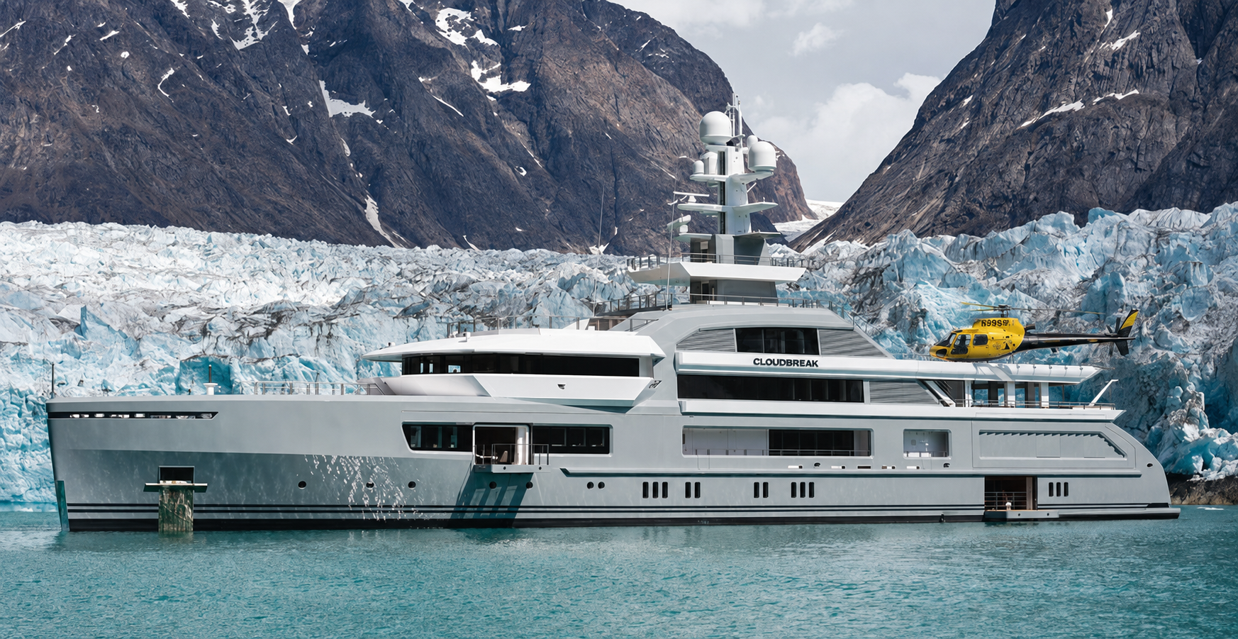 Luxury yacht anchored in a calm Alaskan glacial bay with a helicopter on the rear deck, mountains rising behind